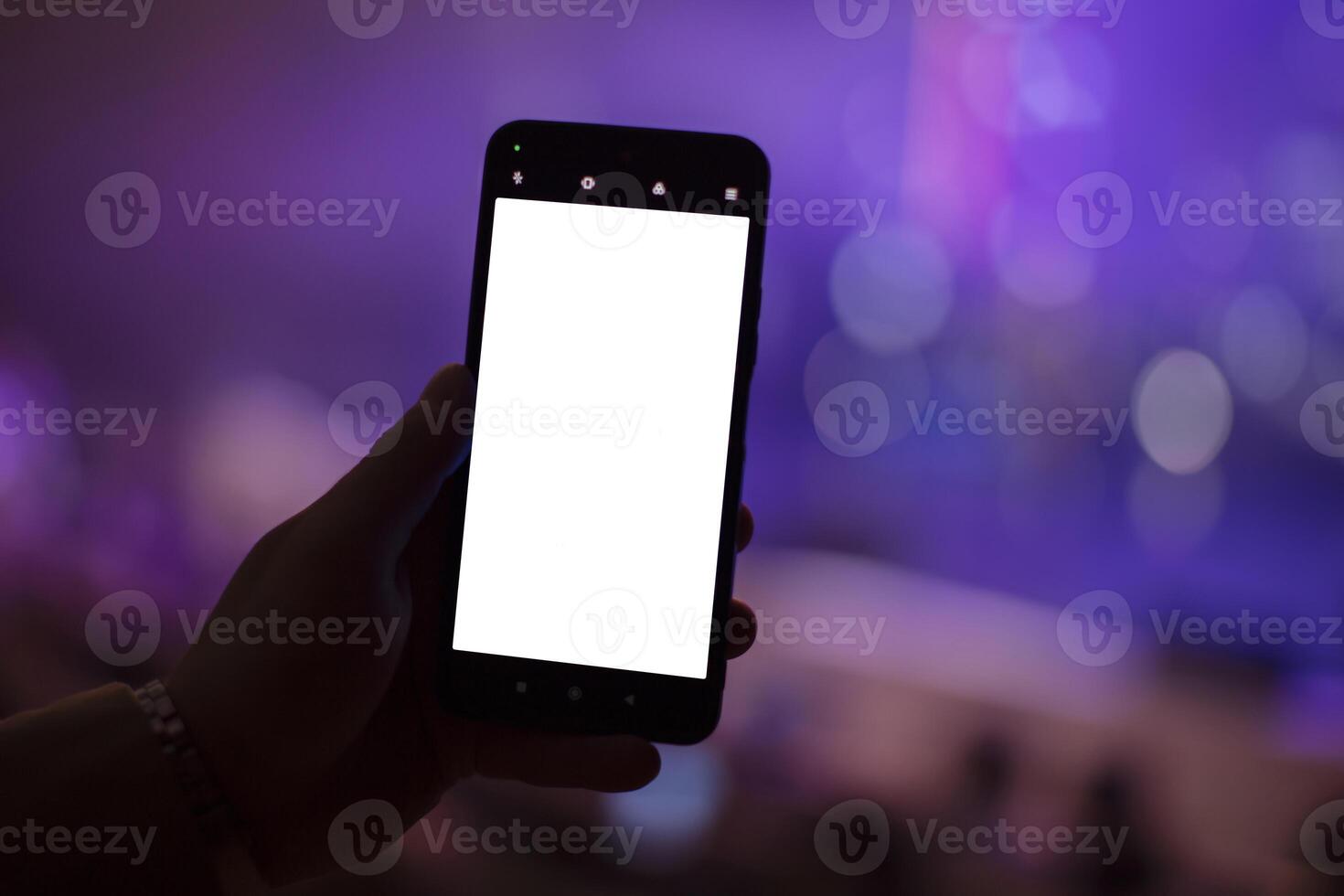 A hand holds a smartphone with a blank screen to copy your text or information content on a dark concert bokeh background. photo