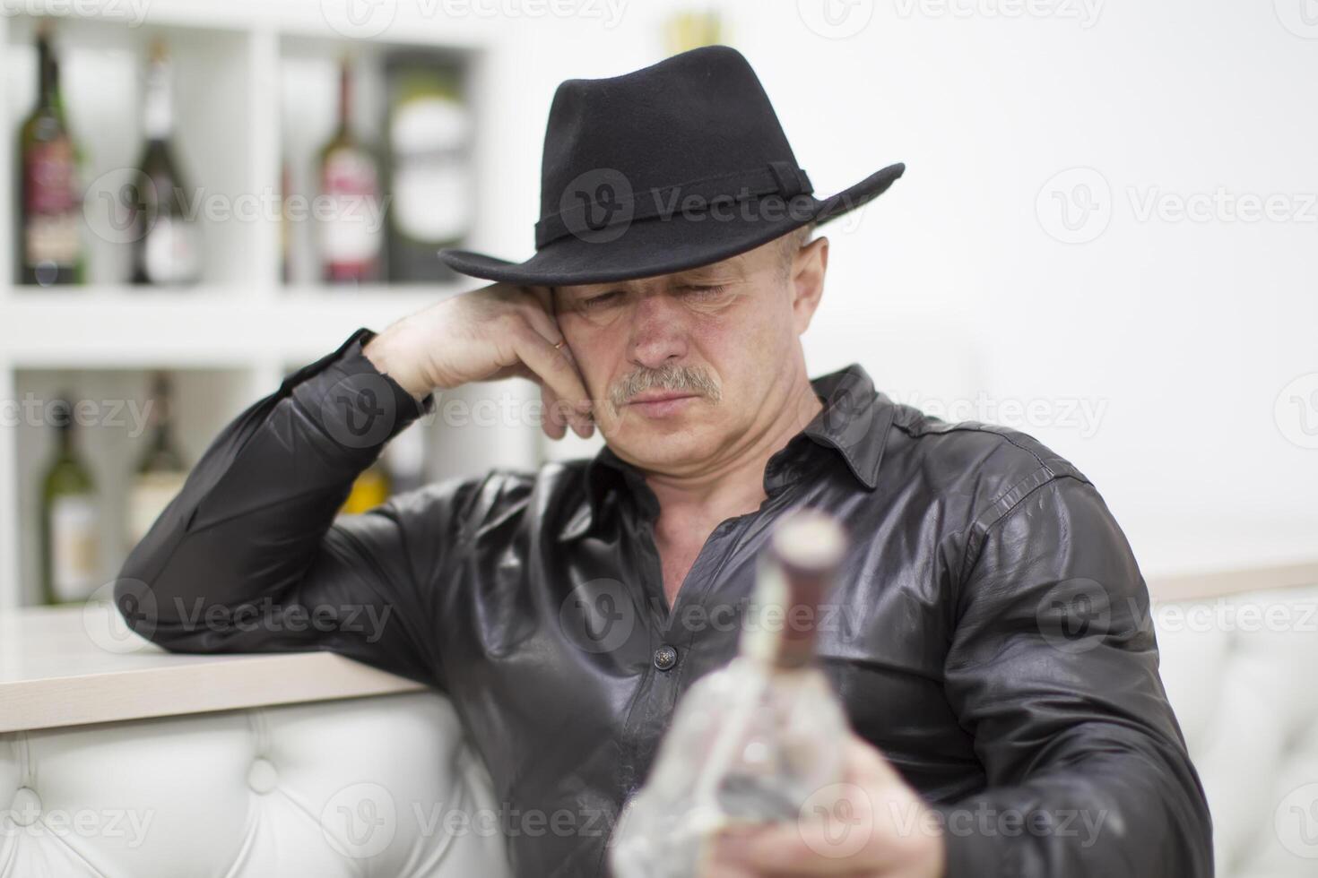 An elderly man in a cowboy hat with a bottle of whiskey. Liquor lover photo