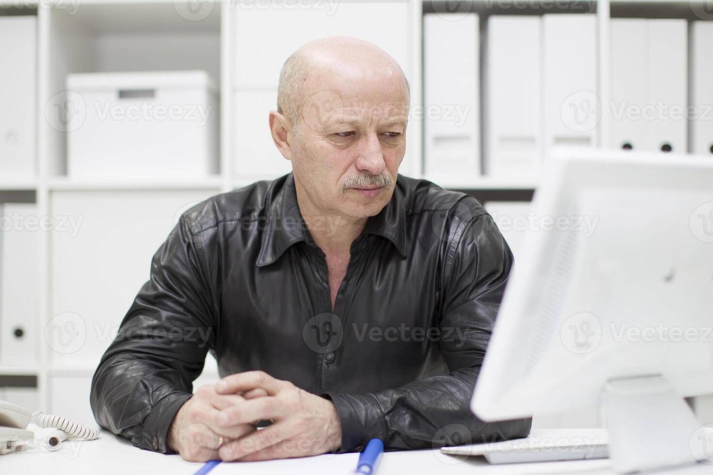 An elderly bald man at the computer. Pensioner in the workplace photo