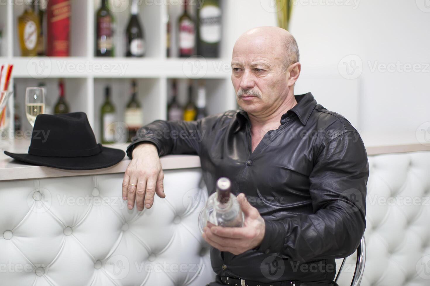 An elderly man with a bottle of whiskey at the bar. Liquor lover photo