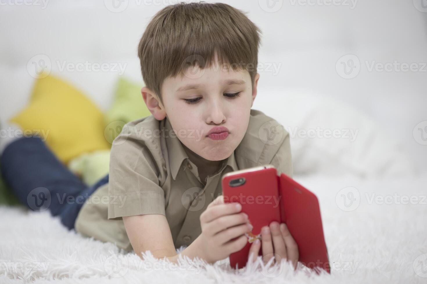 Child with a mobile phone. Schoolboy with a smartphone lying on the bed. Kids and Gadgets photo