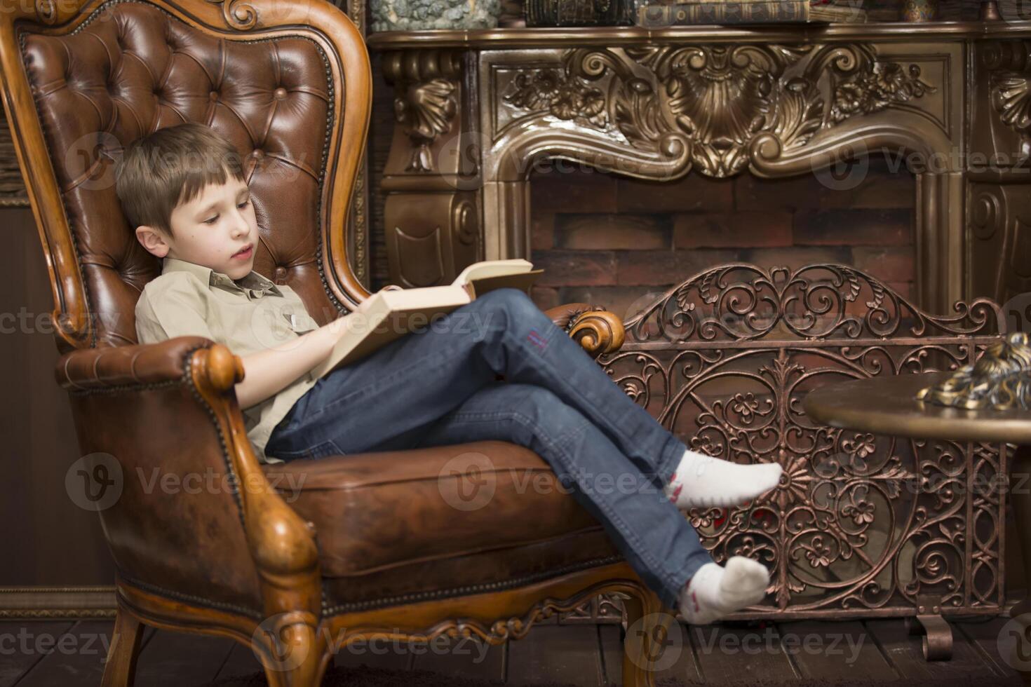 The child in the chair reading a book.Little boy with a book photo