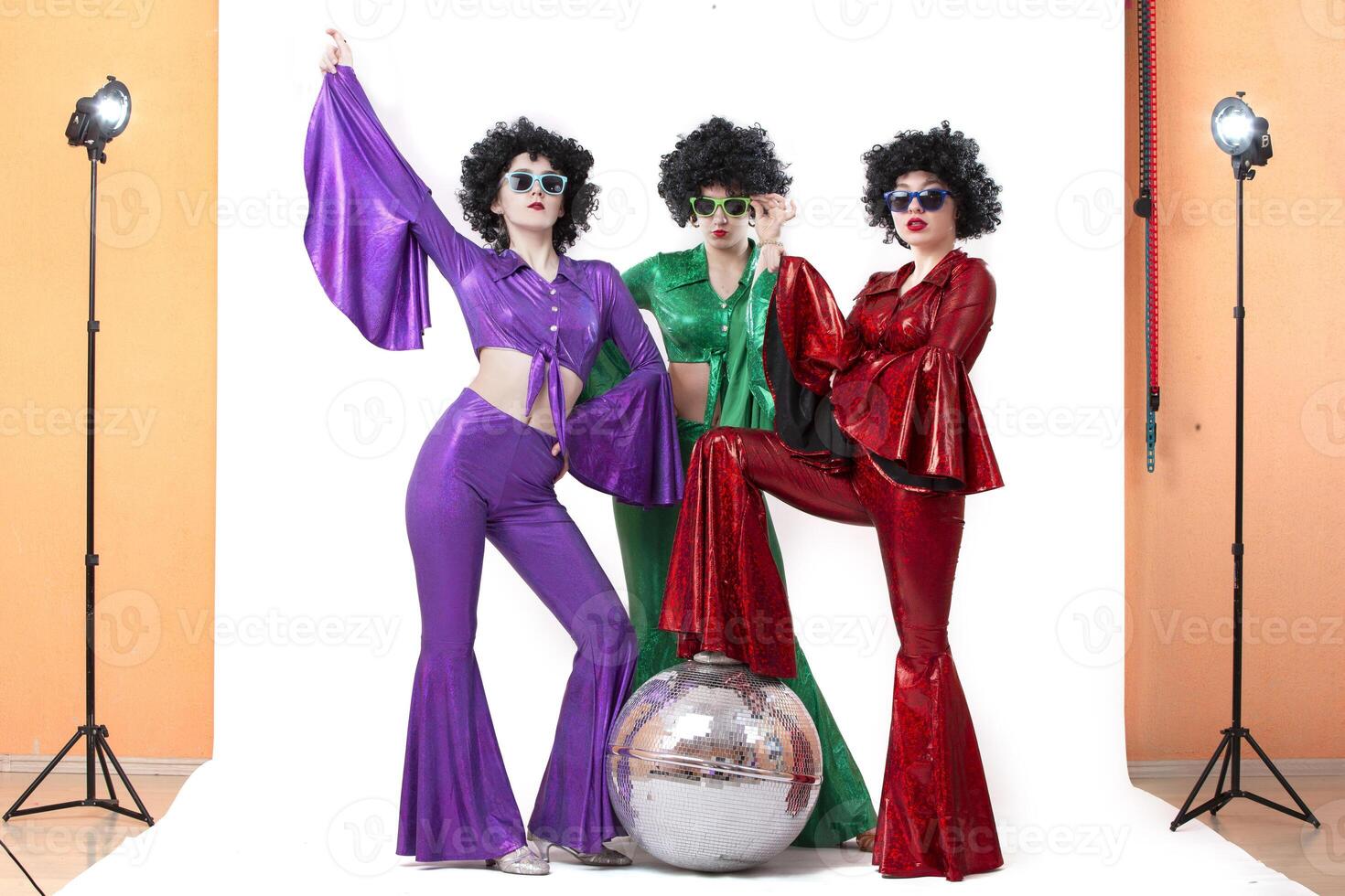 A group of girls with a disco ball in colorful costumes in a photo studio posing on a white background.