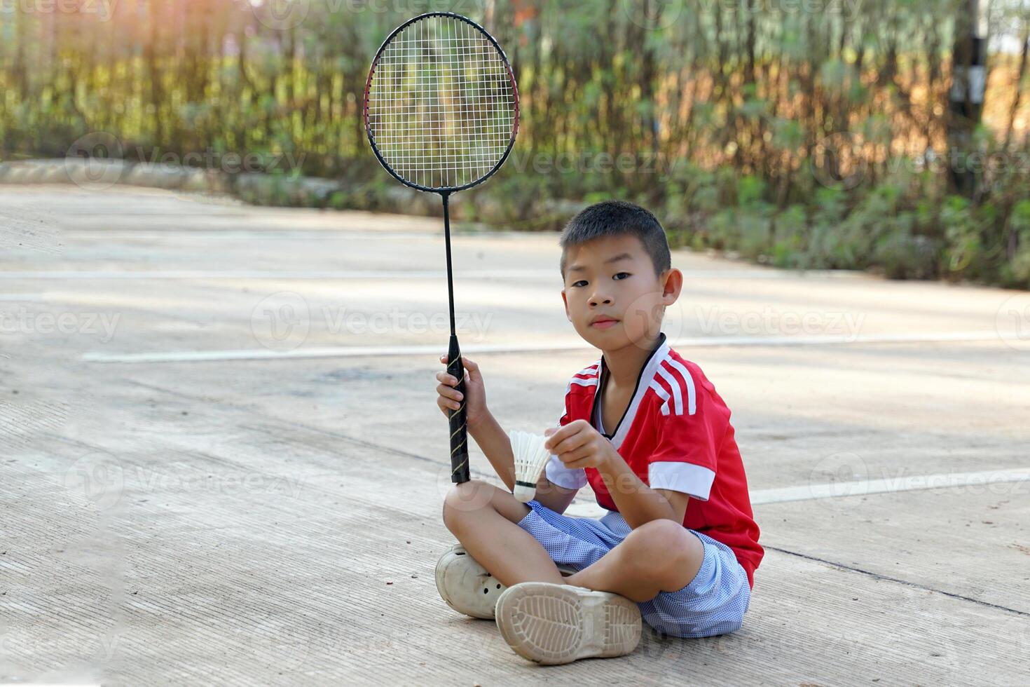 Asian boy sitting cross-legged on the cement floor Hand holding a white shuttlecock. The other hand holds a badminton racket. She rested while playing badminton outside on her day off. photo