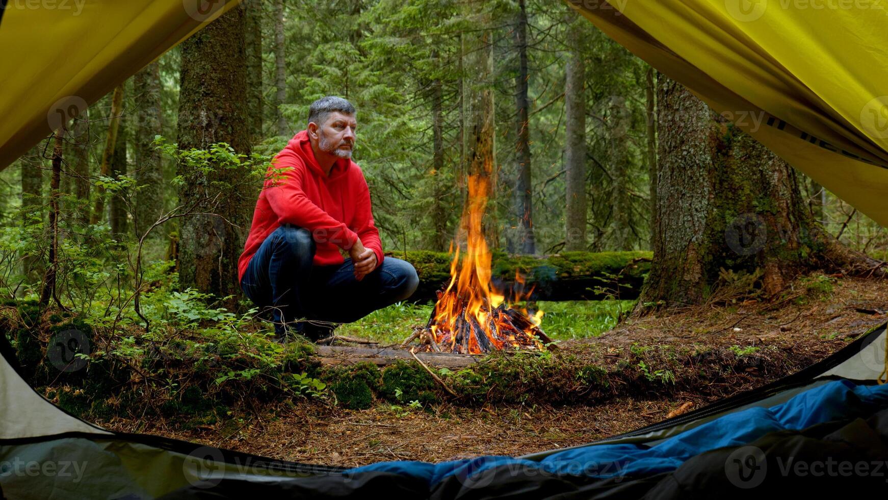 Bearded man by the fire in a beautiful forest. The camping is located in a beautiful forest lawn in the mountains. Travel concept photo