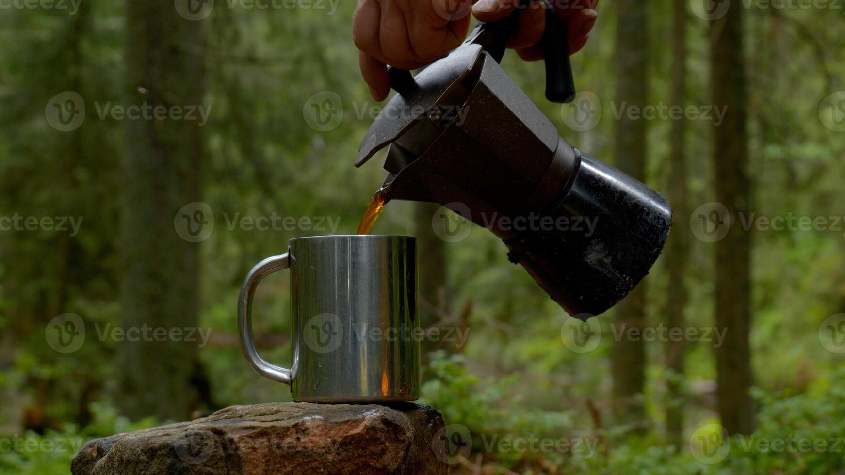 Coffee is poured into a mug from a coffee maker. Beautiful forest on the background. Travel concept Ultra 4K photo