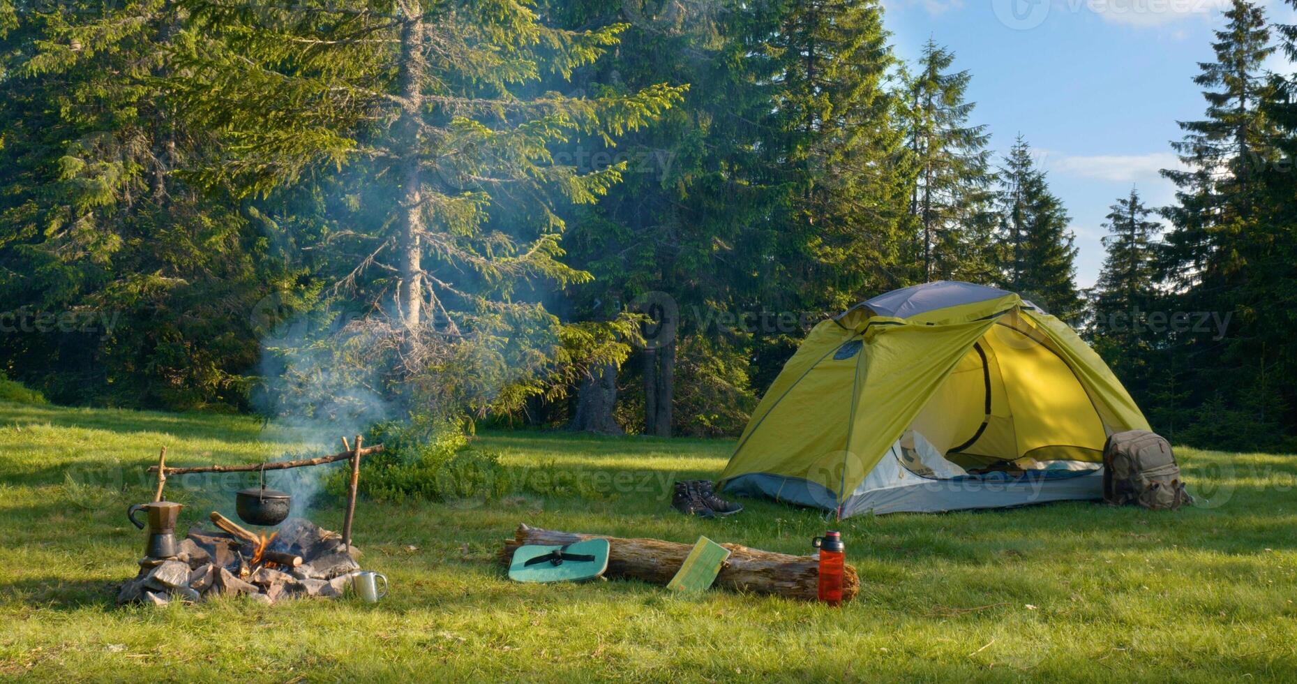 Tent and bonfire on the forest lawn in the mountains. Travel concept photo