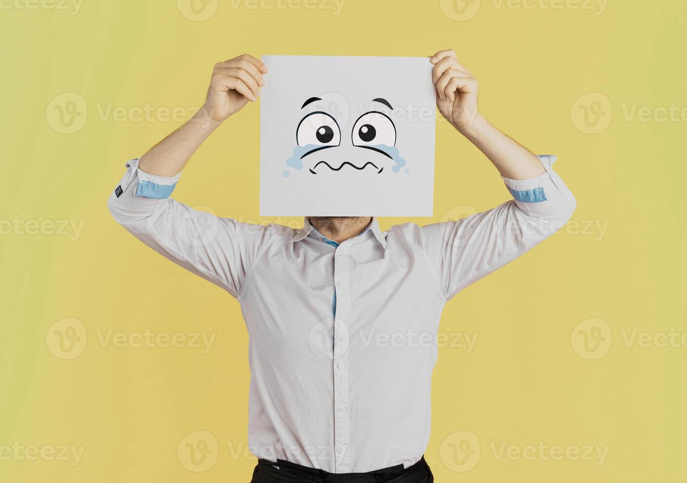 Young businessman holding white card with a sad face on it isolated on Yellow background photo