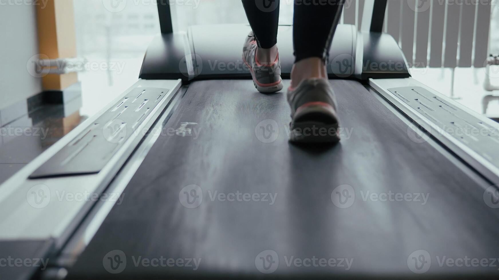 Female legs walking and running on treadmill in gym. Young woman exercising during cardio workout. Feet of girls in sport shoes training indoor at sport club. People jogging. Close up photo