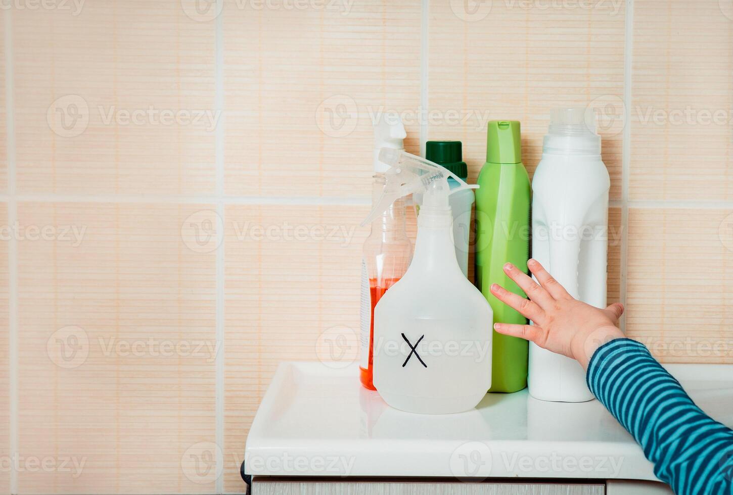 Little child reaches out to household chemicals. Keep away from children. Dangers at home for kids. photo