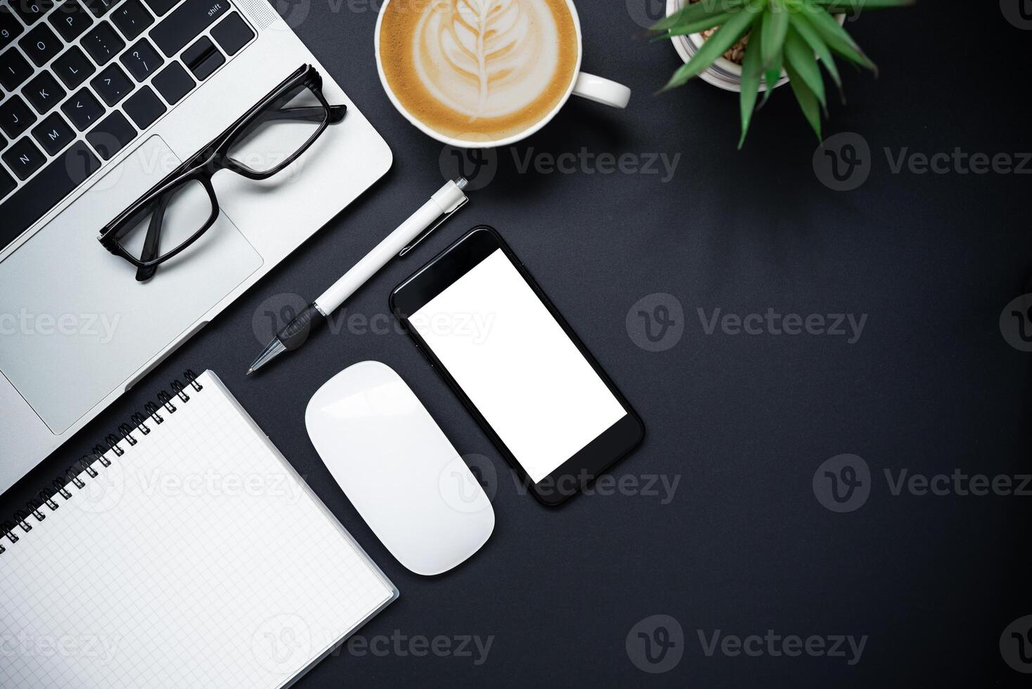 Top view with laptop, mobile phone, coffee cup, pencil, pencil and glasses placed on a black background photo