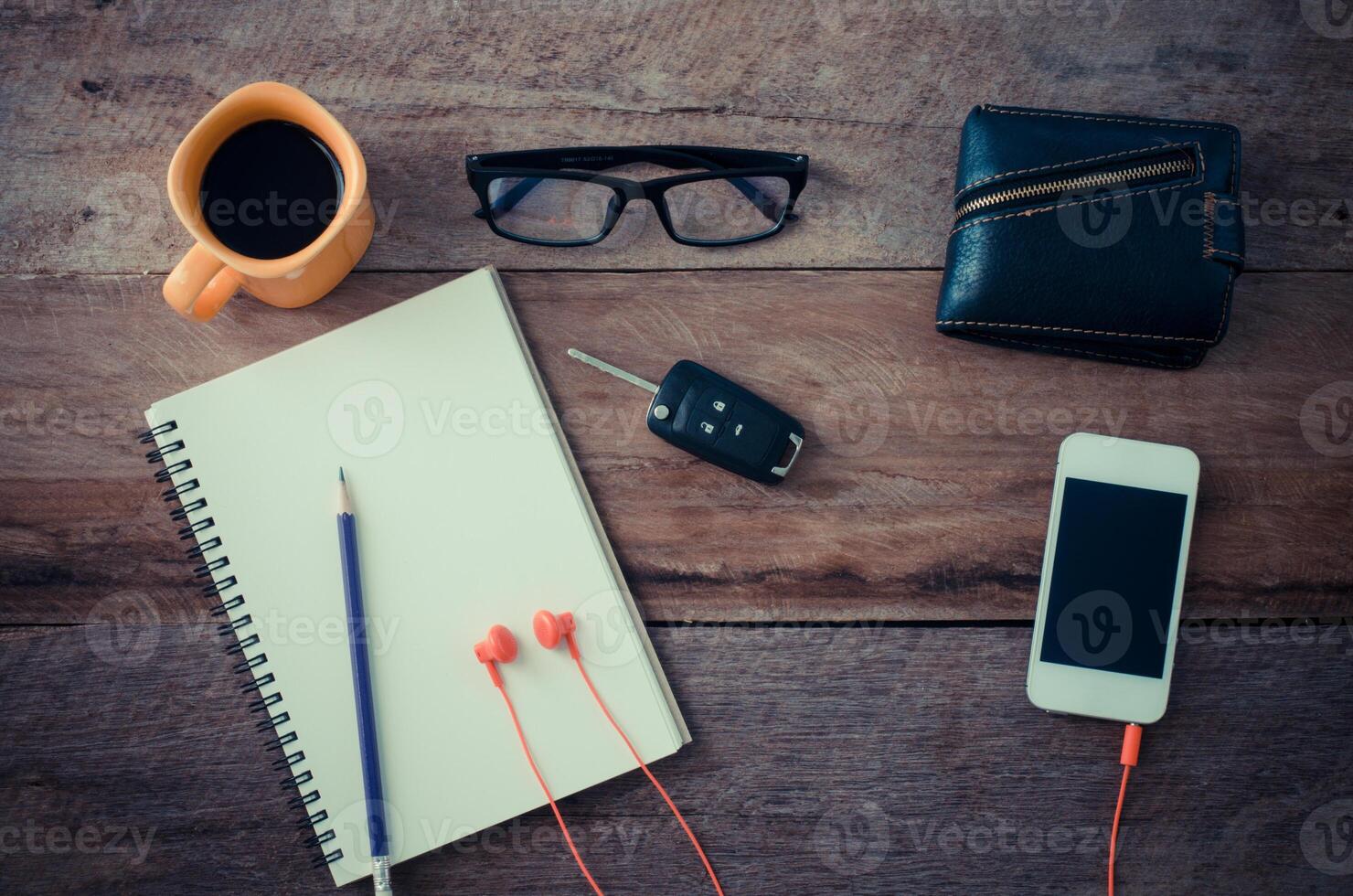 The surface of a wooden table with a notebook, smart-phone, glasses, wallet, car keys, coffee cup photo