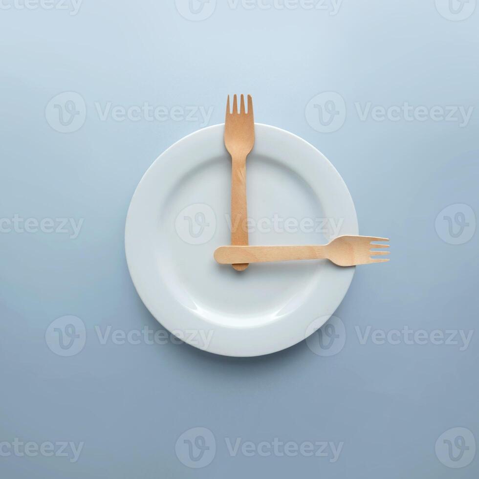 Top view of Spoon and fork on white round plate in a form of clock on blue background. Minimal food idea concept. photo