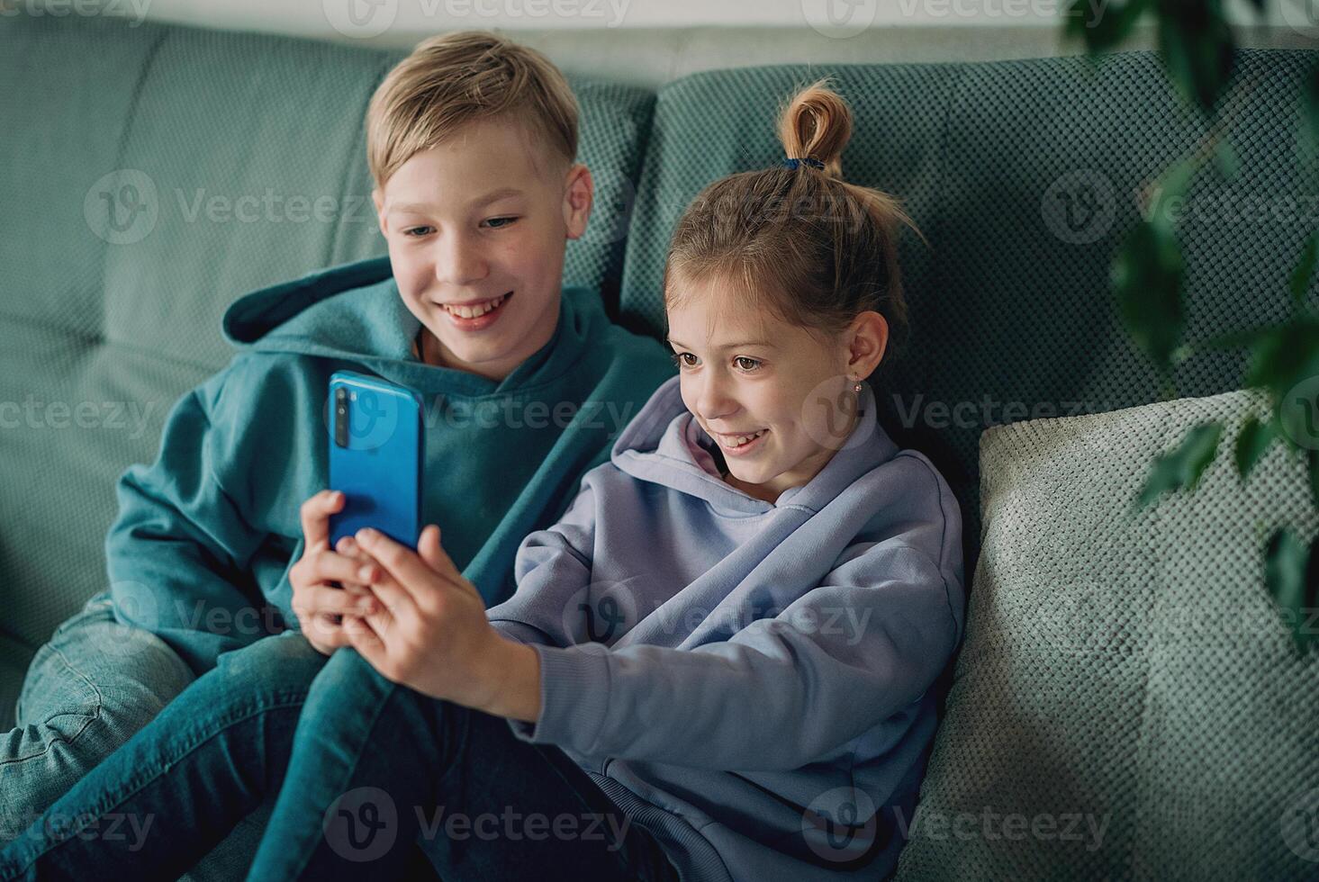 two children sitting on a couch looking at a phone photo