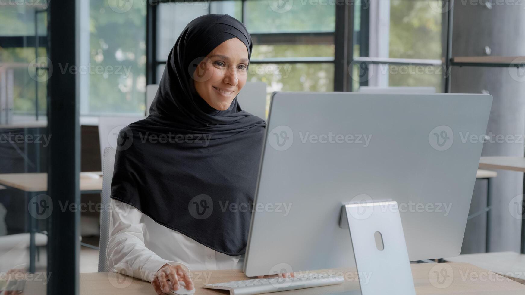 Happy successful arab businesswoman in hijab typing on keyboard working on computer enjoying work online in modern office smiling female manager placing order on Internet communicates on social media photo