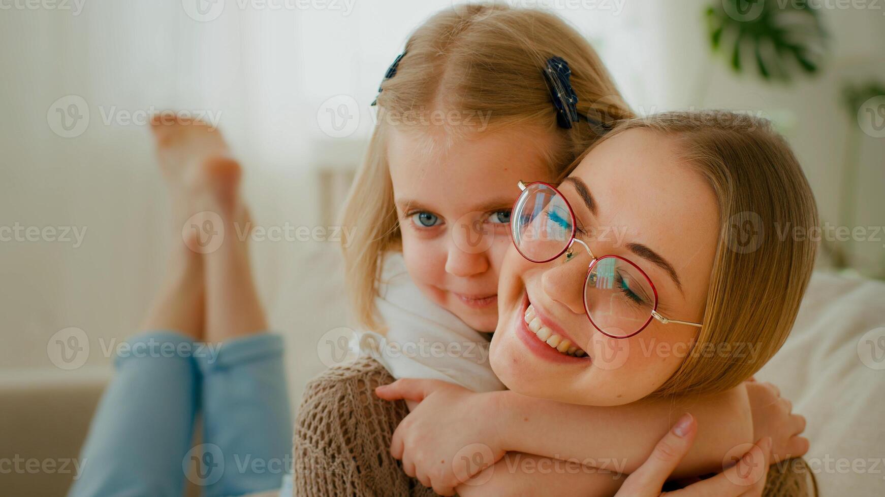 caucásico familia cercanía. pequeño linda hija niño bebé niña abrazo abrazo abrazo mamá por cuello a cuestas acostado juntos a hogar amor relación niño abrazando abrazando acurrucarse madre en los anteojos foto