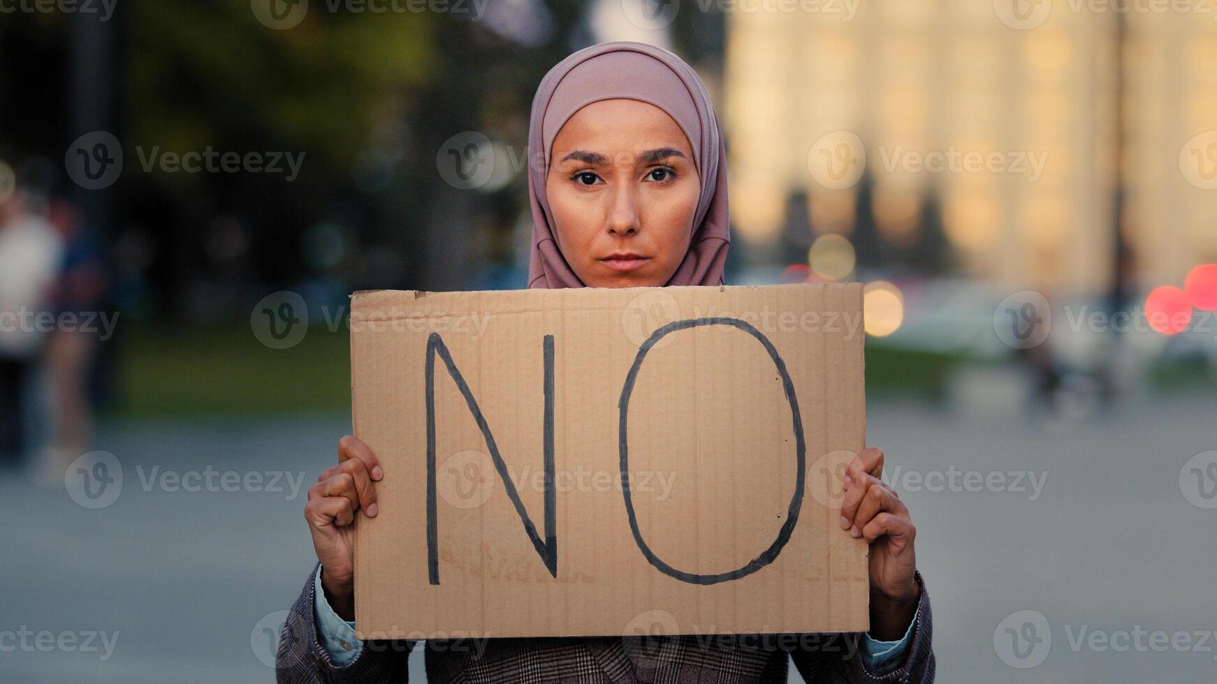 Stop racism No concept Arab immigrant Muslim woman in hijab protests against discrimination vax vaccination standing in city. Islamic girl holding cardboard slogan banner with text no disagree refusal photo