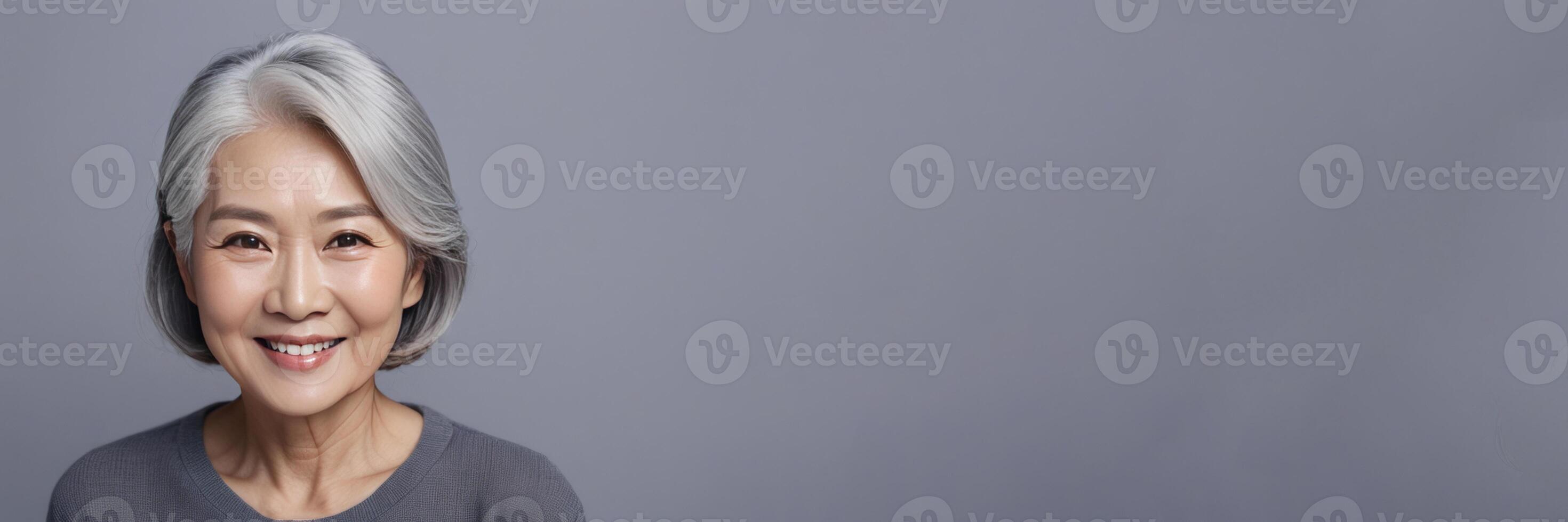 AI generated A portrait of an Asian lady, a smiling elderly woman with gray hair, stands on a gray background. A place for text, a banner for advertising. photo