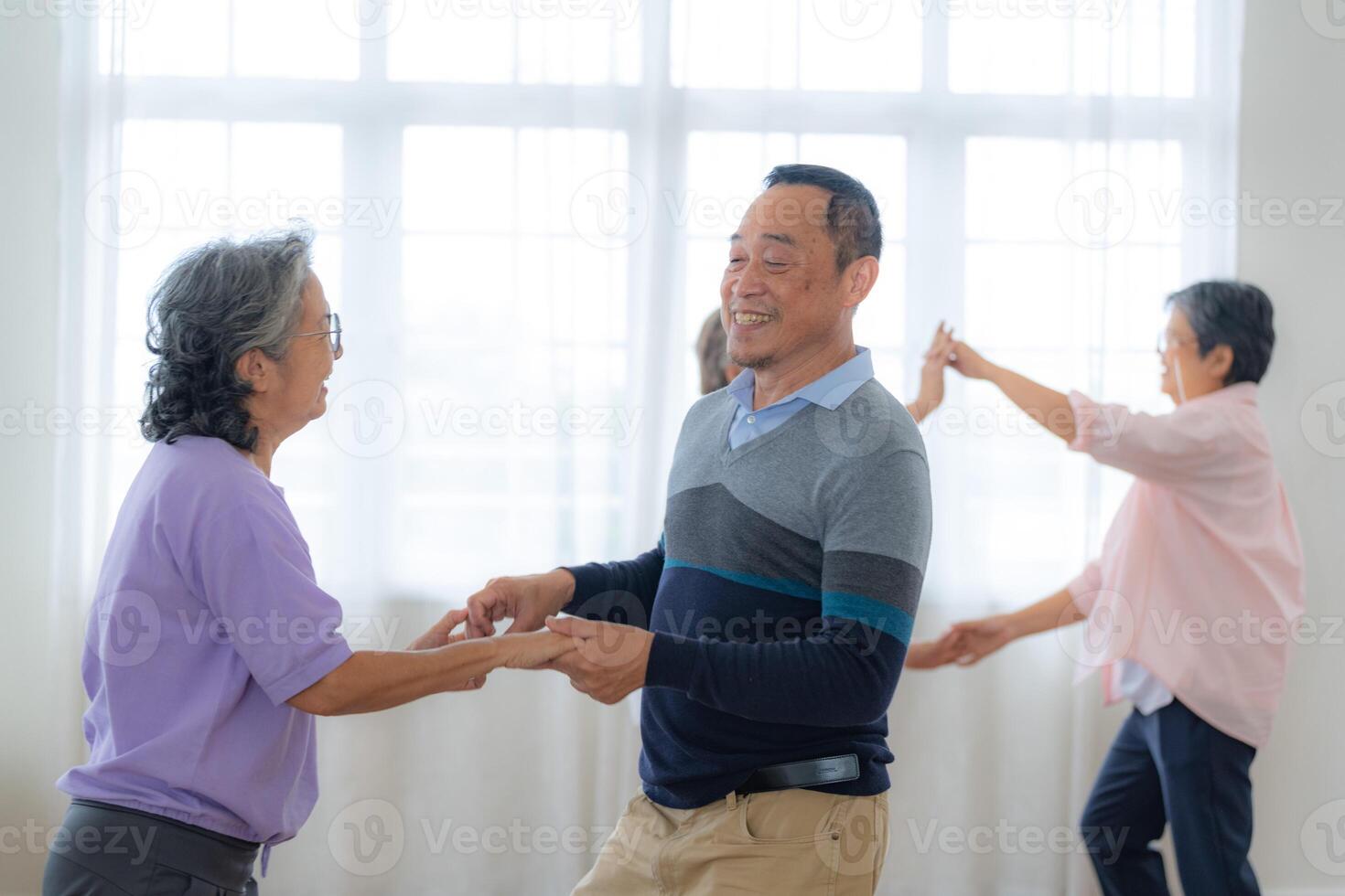 Asian Older male and females people dance with their partners on a dancing floor in living space. Happy older couple performing get exercise. Joyful carefree retired senior friends enjoying relaxation photo