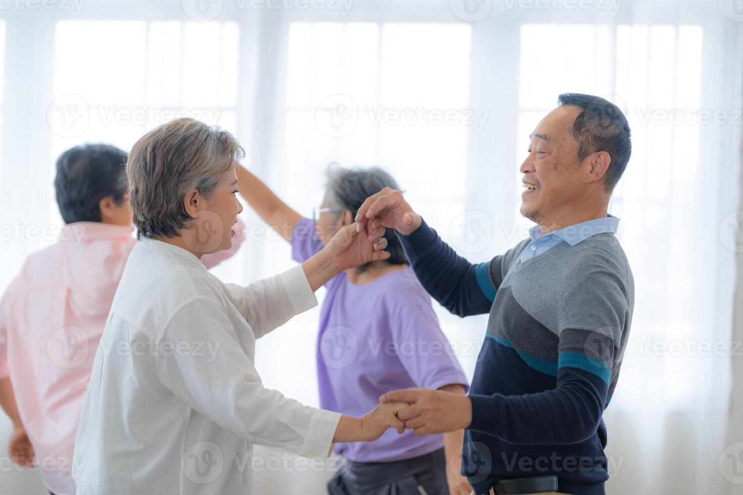 Asian Older male and females people dance with their partners on a dancing floor in living space. Happy older couple performing get exercise. Joyful carefree retired senior friends enjoying relaxation photo