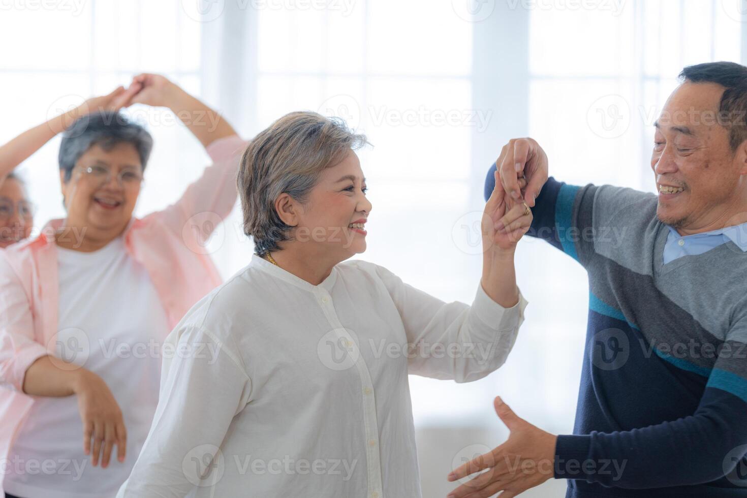 Asian Older male and females people dance with their partners on a dancing floor in living space. Happy older couple performing get exercise. Joyful carefree retired senior friends enjoying relaxation photo