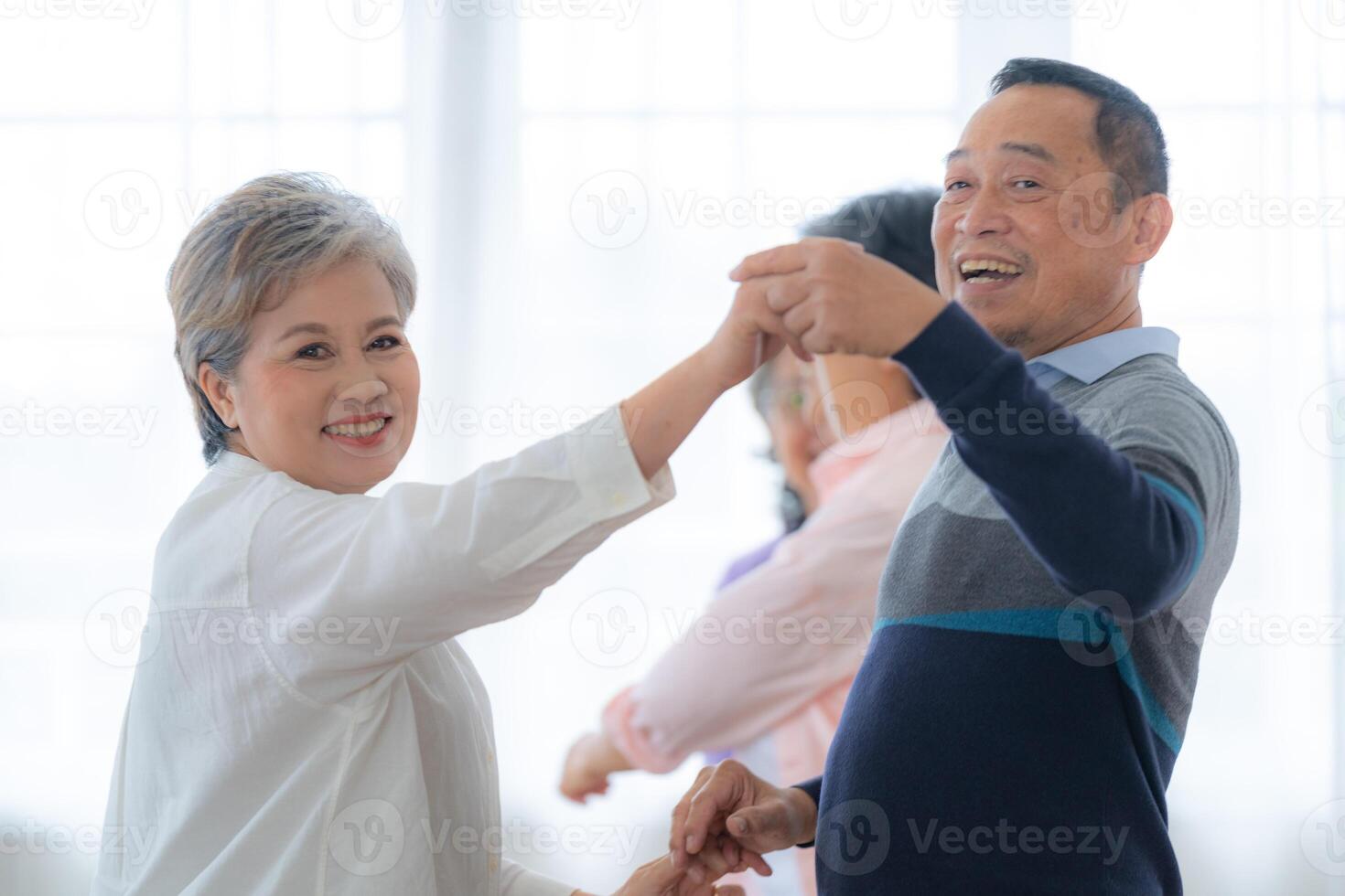 Asian Older male and females people dance with their partners on a dancing floor in living space. Happy older couple performing get exercise. Joyful carefree retired senior friends enjoying relaxation photo