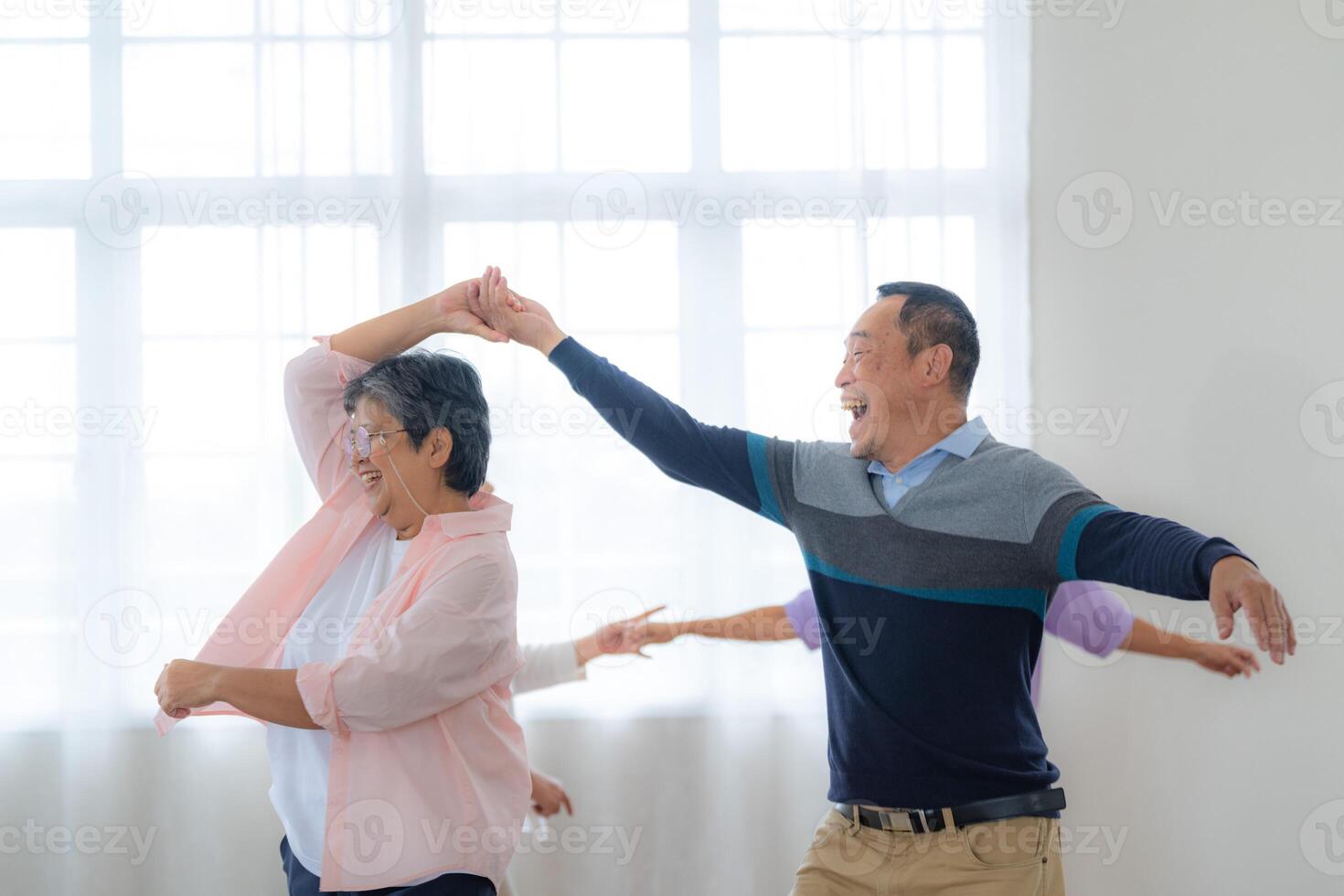 Asian Older male and females people dance with their partners on a dancing floor in living space. Happy older couple performing get exercise. Joyful carefree retired senior friends enjoying relaxation photo