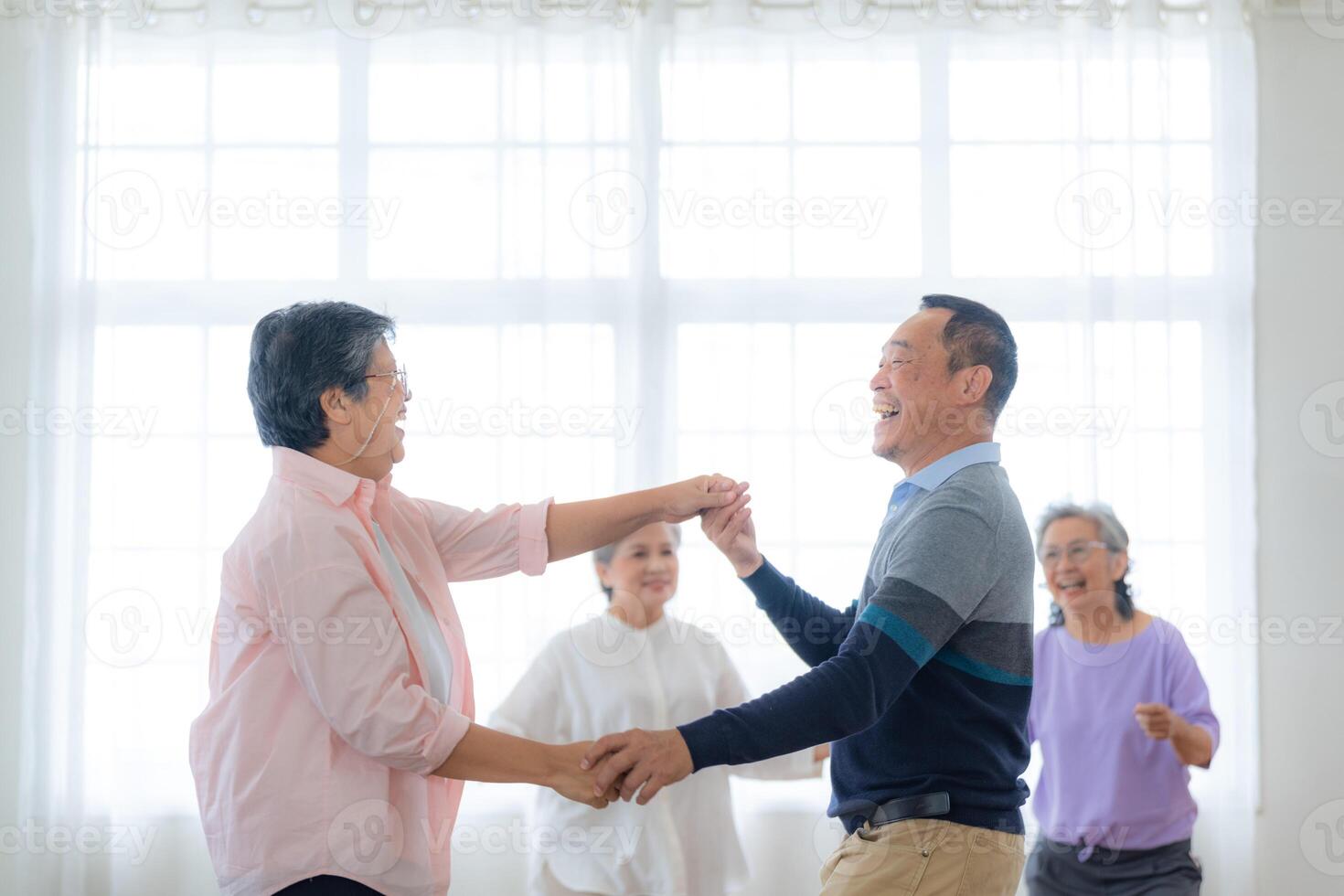 Asian Older male and females people dance with their partners on a dancing floor in living space. Happy older couple performing get exercise. Joyful carefree retired senior friends enjoying relaxation photo