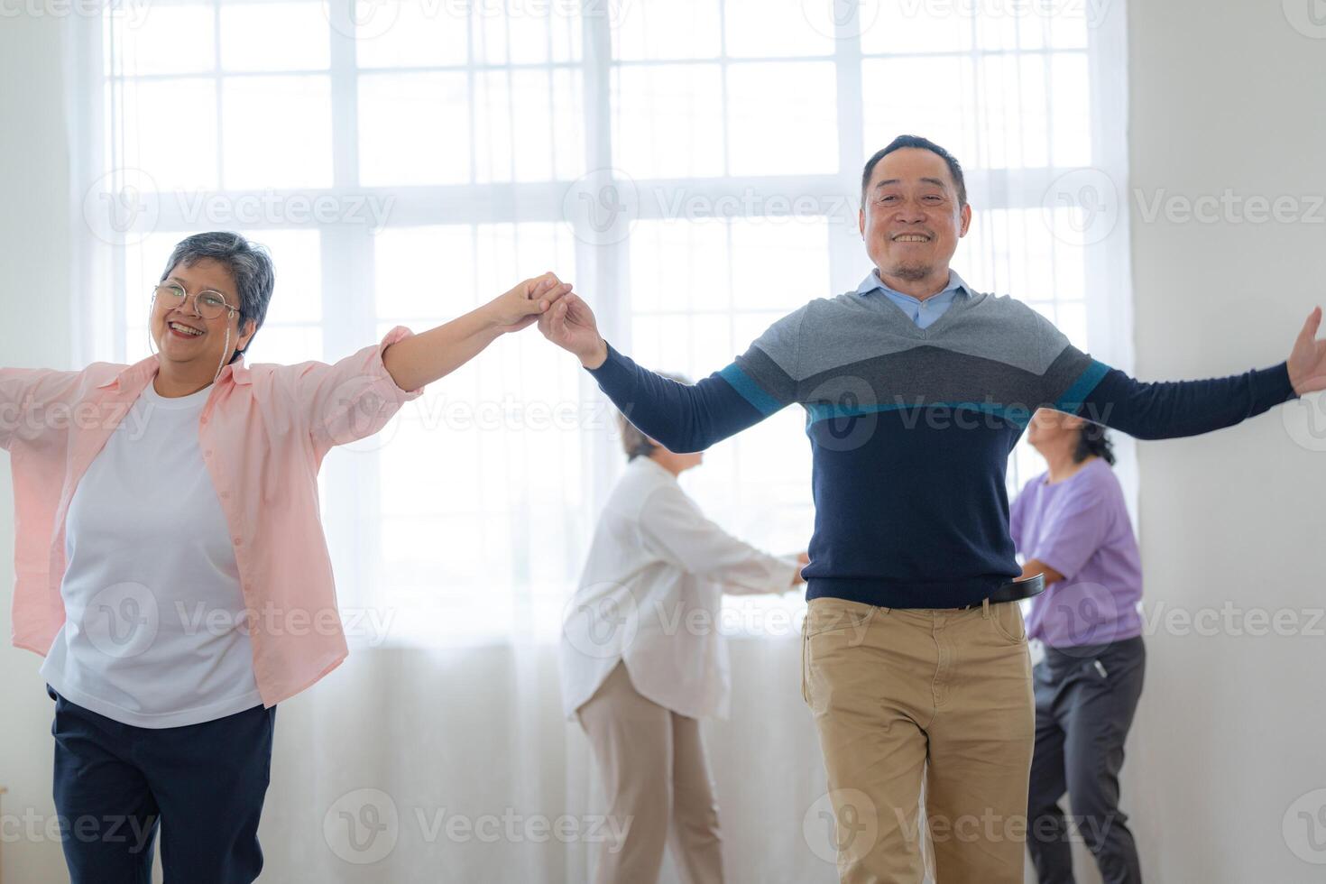 Asian Older male and females people dance with their partners on a dancing floor in living space. Happy older couple performing get exercise. Joyful carefree retired senior friends enjoying relaxation photo