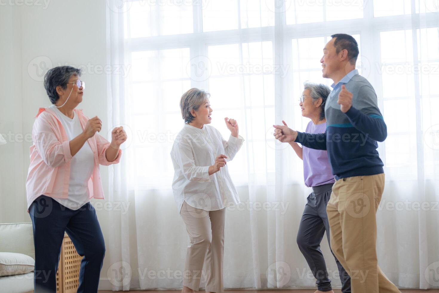 Asian Older male and females people dance with their partners on a dancing floor in living space. Happy older couple performing get exercise. Joyful carefree retired senior friends enjoying relaxation photo