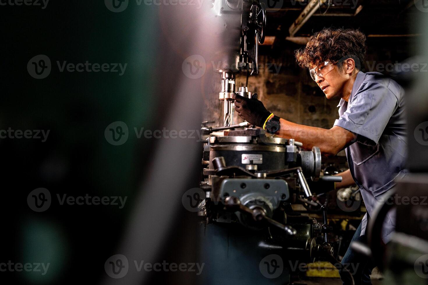 asiático trabajador en producción planta perforación a máquina. profesional trabajador cerca perforación máquina en fábrica. refinamiento metal trabajando interno acero superficie en torno amoladora máquina con volador chispas. foto