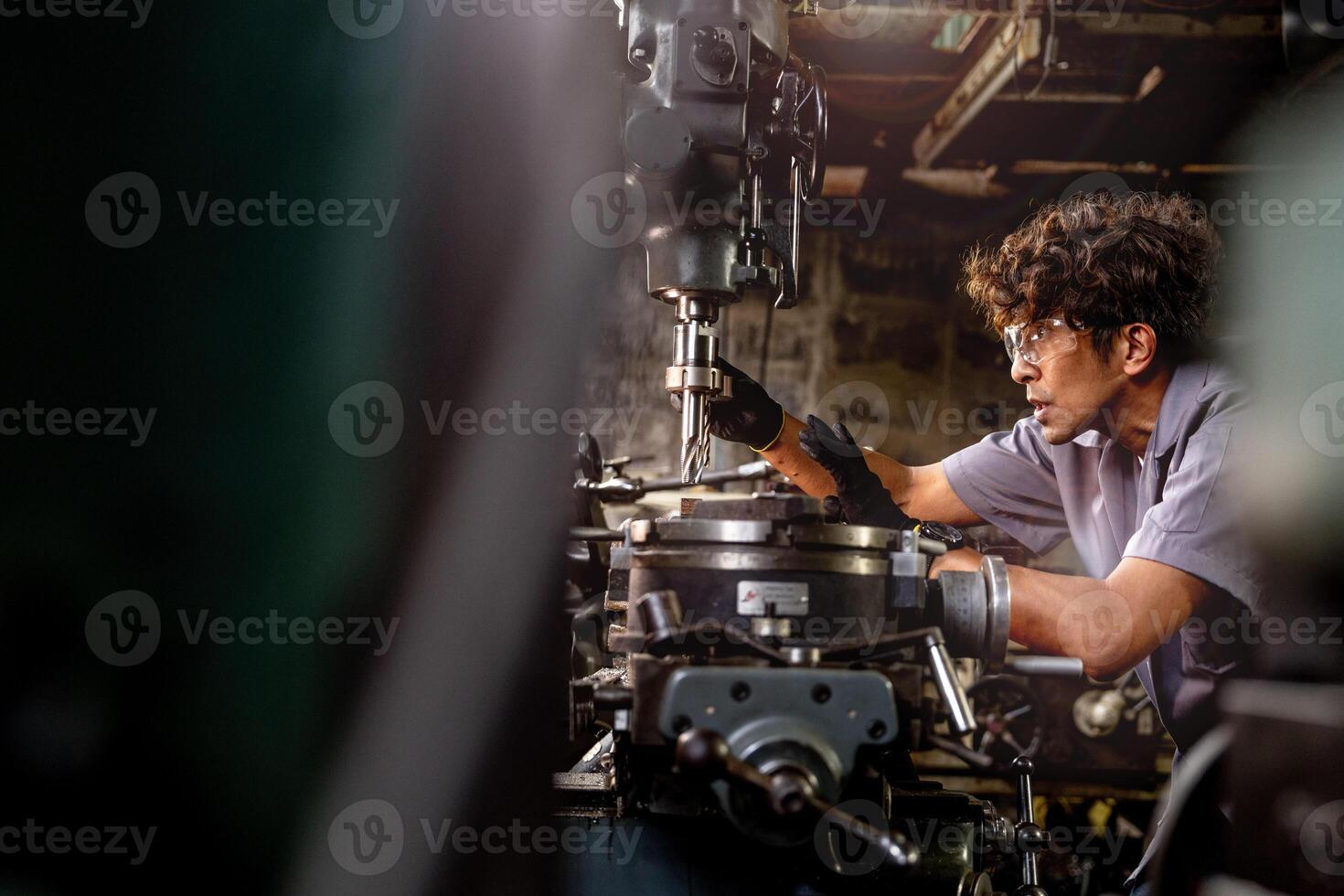 Asian worker in production plant drilling at machine. Professional worker near drilling machine on factory. finishing metal working internal steel surface on lathe grinder machine with flying sparks. photo