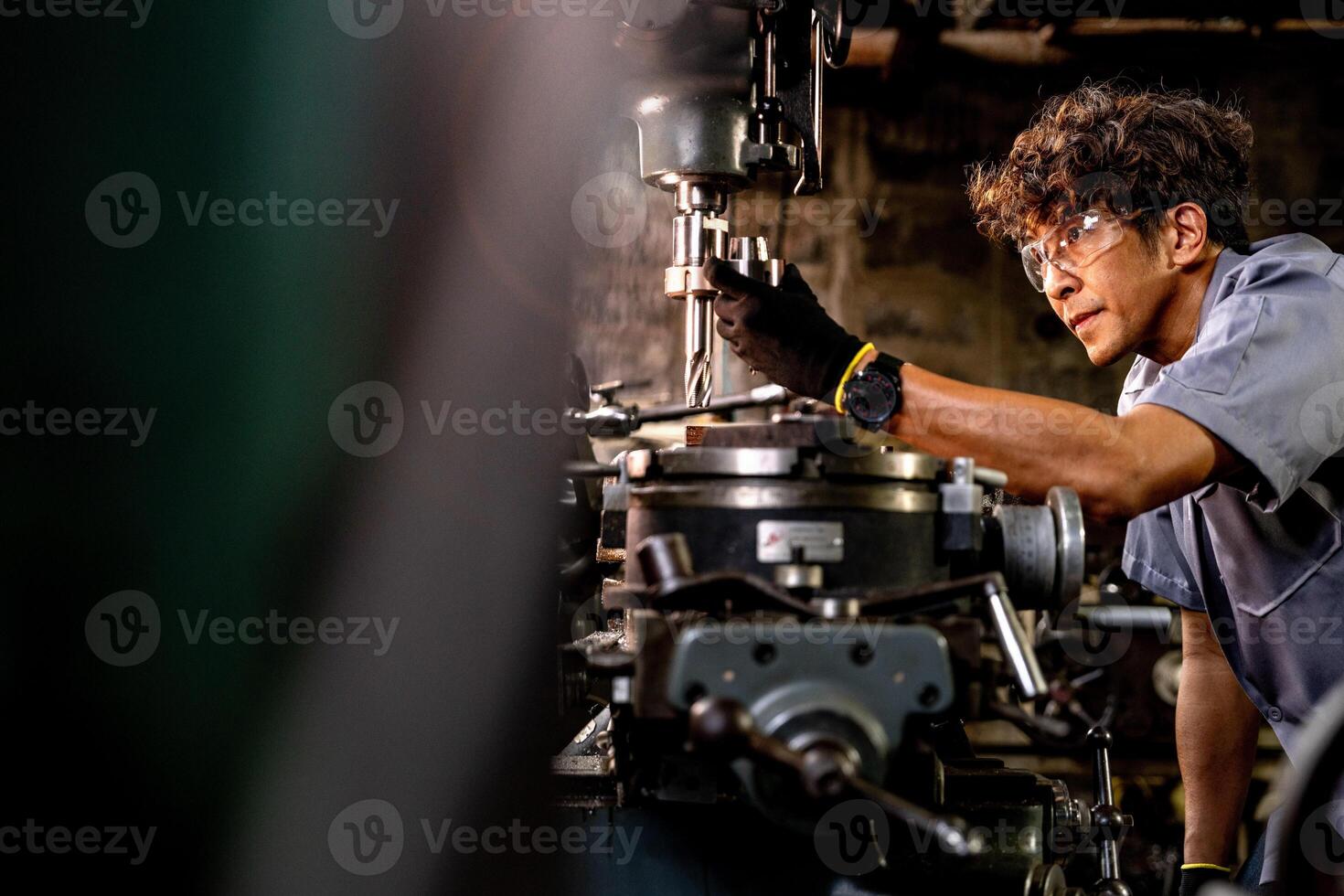 Asian worker in production plant drilling at machine. Professional worker near drilling machine on factory. finishing metal working internal steel surface on lathe grinder machine with flying sparks. photo