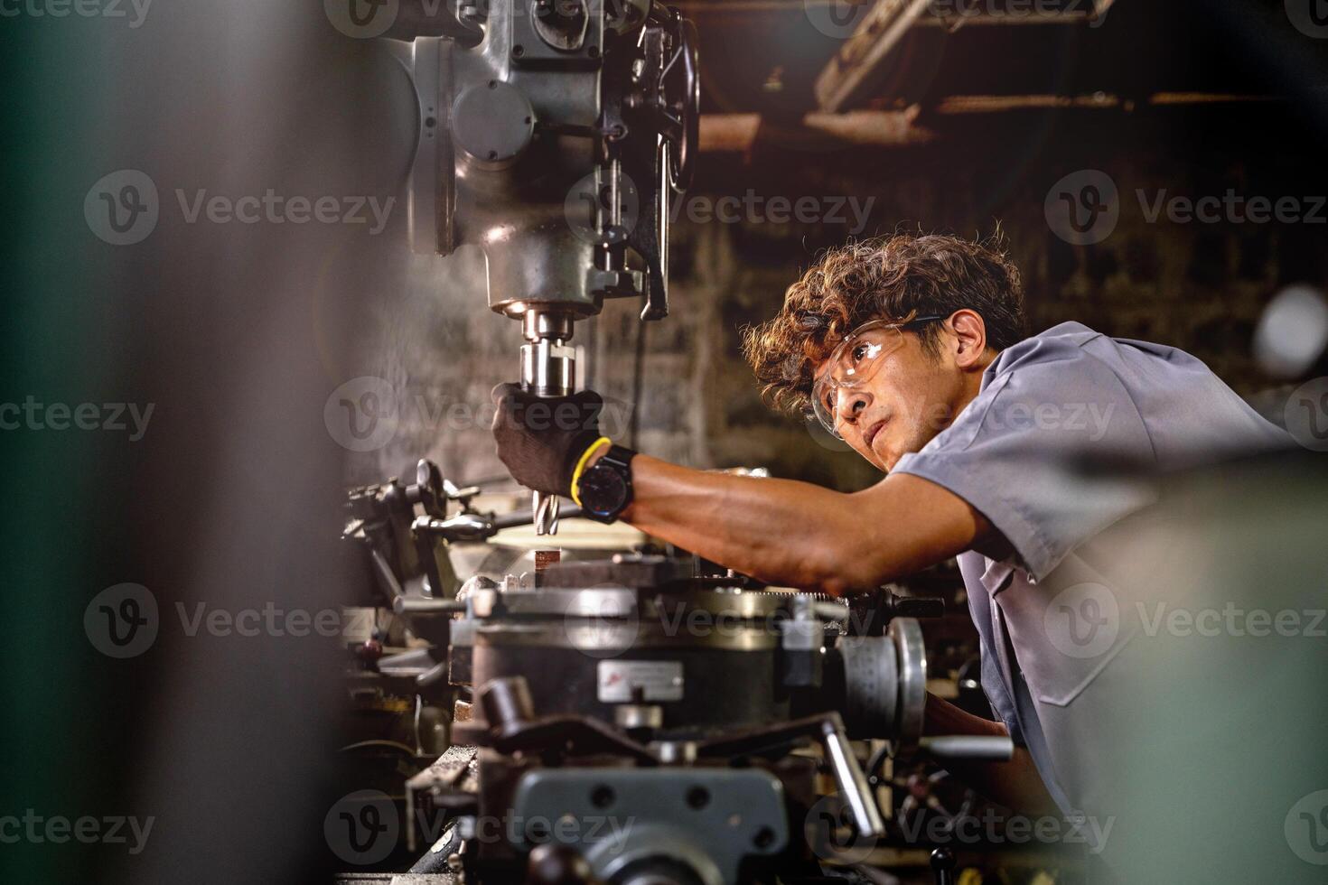 Asian worker in production plant drilling at machine. Professional worker near drilling machine on factory. finishing metal working internal steel surface on lathe grinder machine with flying sparks. photo