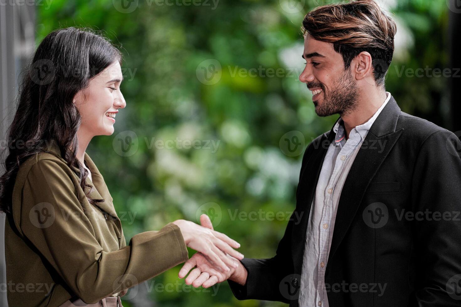 empresario y casual mujer de negocios sacudida manos al aire libre. dos joven multicultural compañeros de trabajo acuerdo para éxito. antecedentes de verde pared naturaleza arboles foto