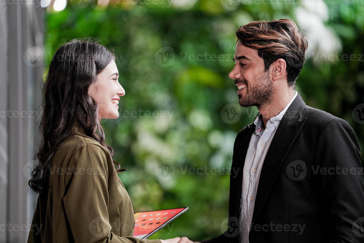 Businessman and casual businesswoman shaking hands outdoors. Two young multicultural coworkers deal for success. background of  green wall nature trees. photo