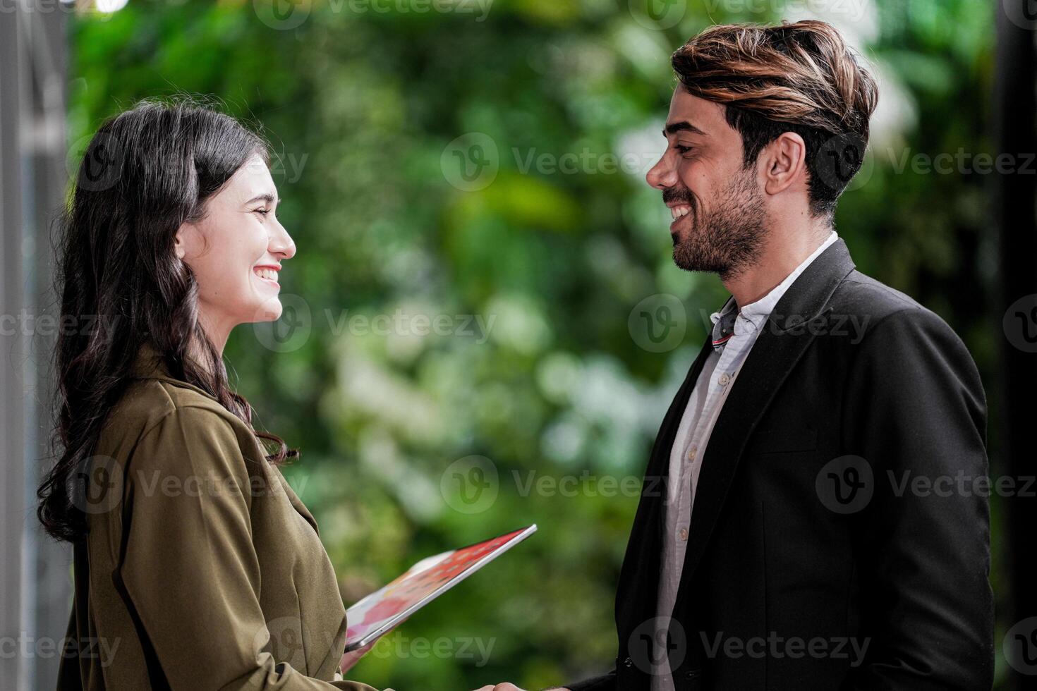 Businessman and casual businesswoman shaking hands outdoors. Two young multicultural coworkers deal for success. background of  green wall nature trees. photo