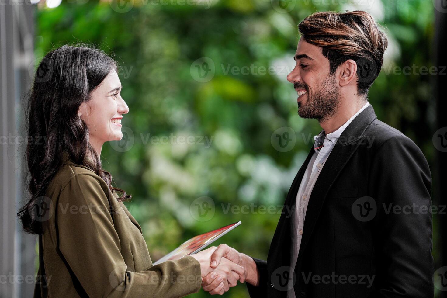 Businessman and casual businesswoman shaking hands outdoors. Two young multicultural coworkers deal for success. background of  green wall nature trees. photo