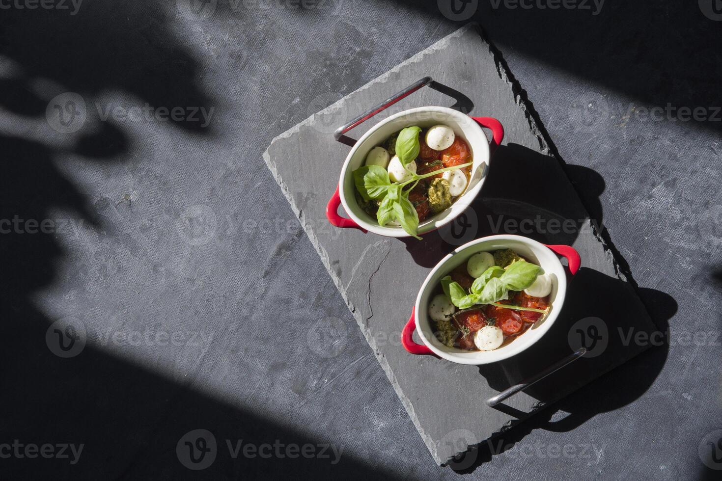 horneado Cereza Tomates en en porciones sartenes debajo luz de sol en el mesa plana poner, difícil luz, ingrediente para caprese apetito foto