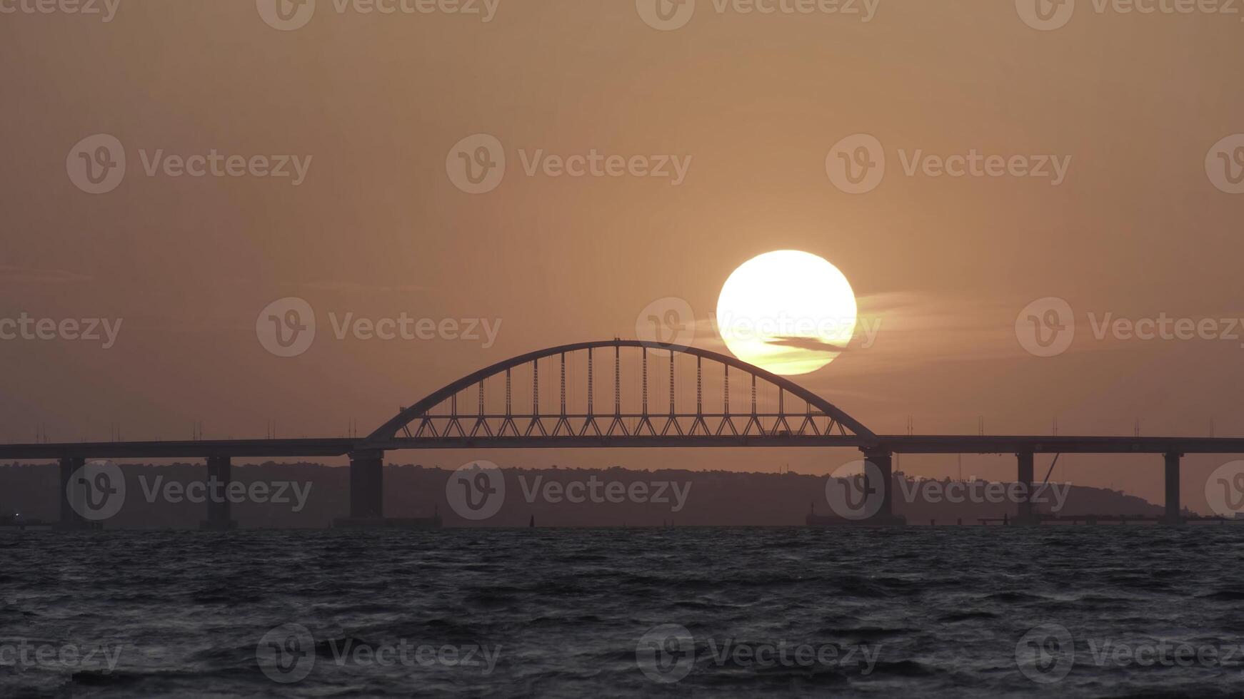 Stunning view of the beautiful sunset over the big river and the bridge, time lapse effect. Shot. Bright golden sun moving towards the horizon above the river. photo