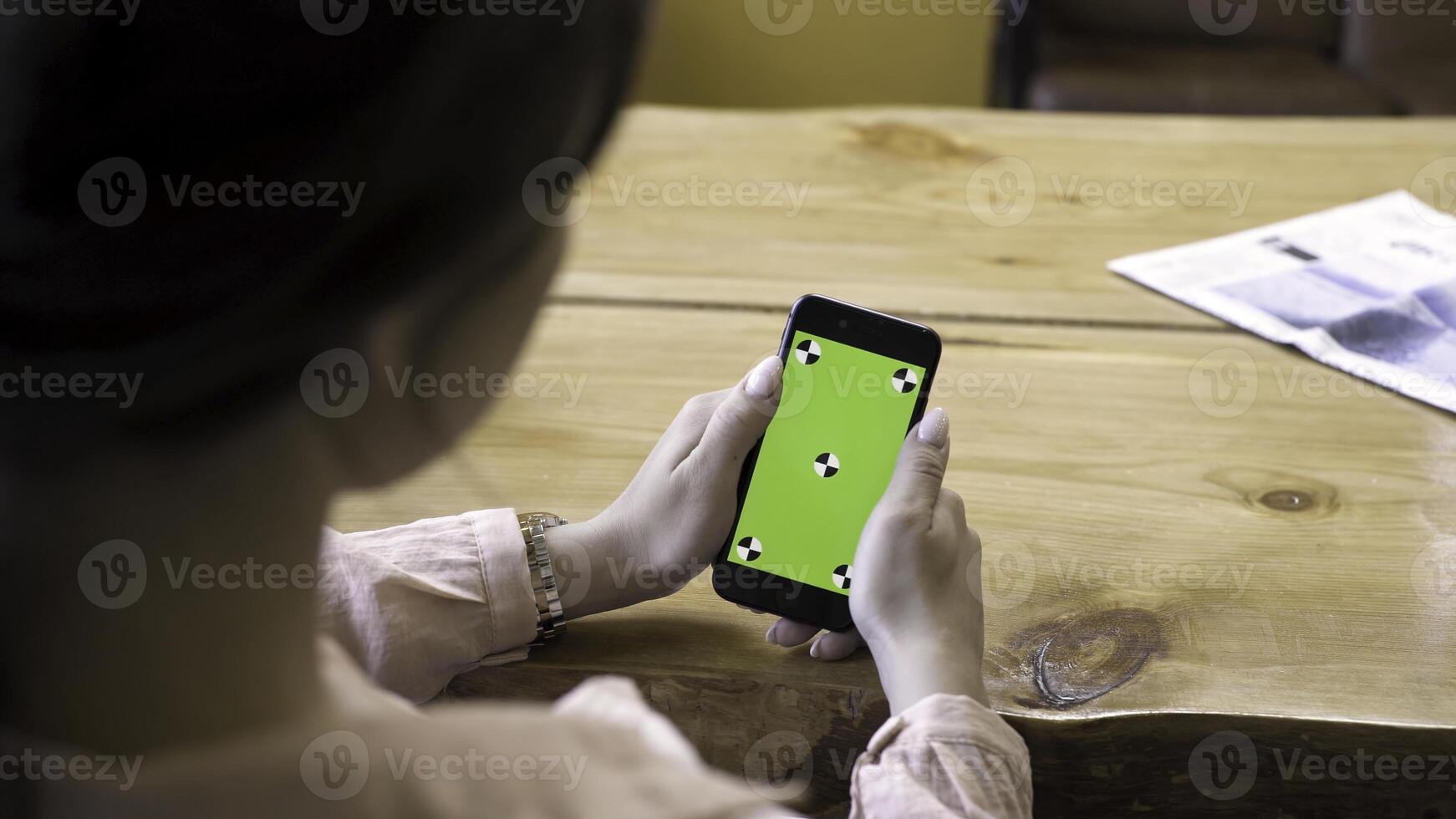 Close up of girl sitting at the table and using smartphone with green screen. Stock footage. View over the shoulder of a woman on the device with chromakey. photo