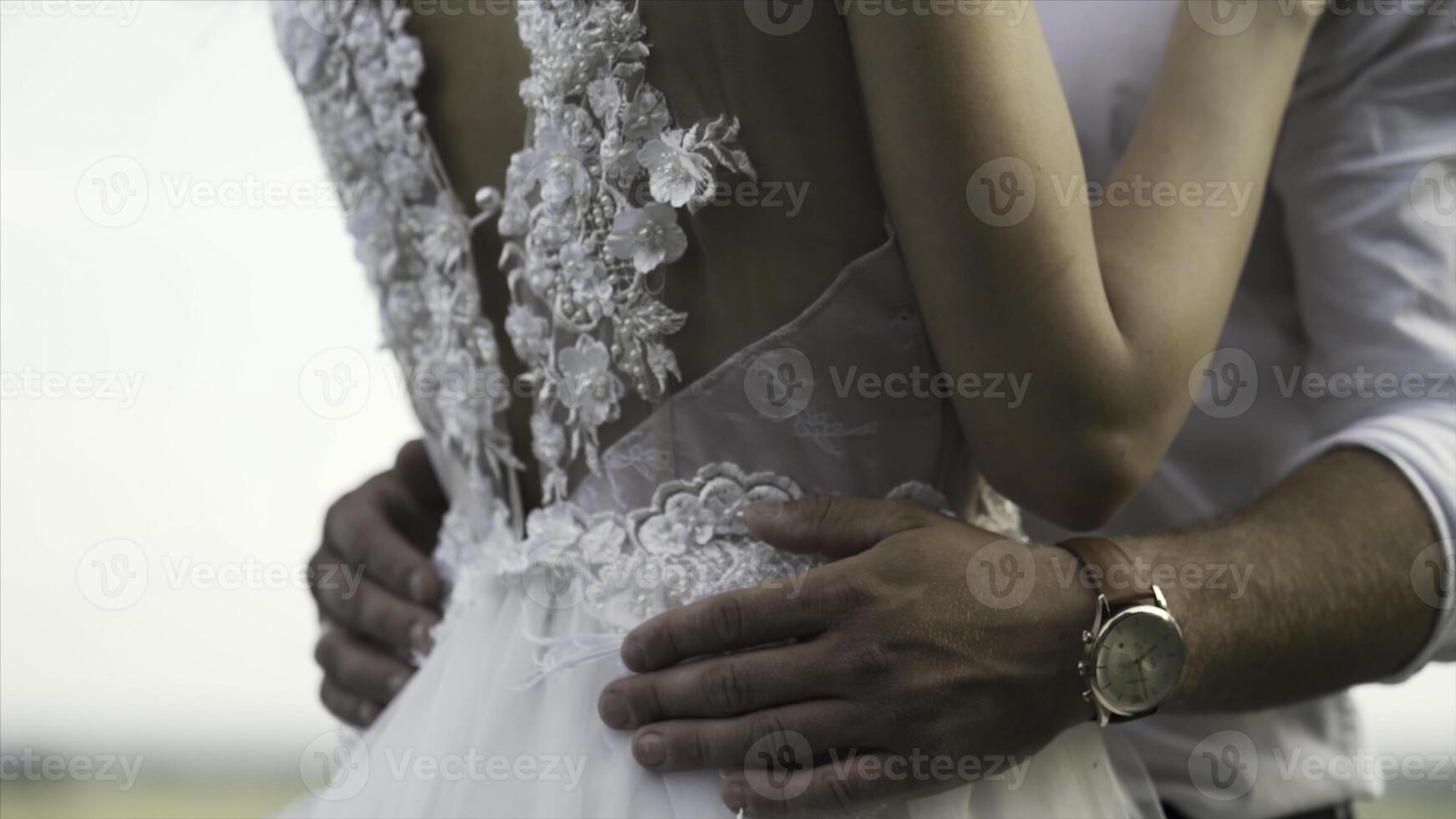 Rear view of a beautiful white wedding dress of a young slim bride with gentle flowers and cutout back. Action. Loving ang hugging bride and groom on bright sky background. photo
