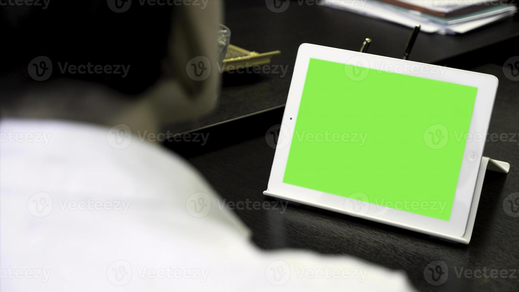 Close up for a woman looking at a white tablet with a green screen. Girl in white shirt working in office in front of tablet with chroma key, rear view. photo