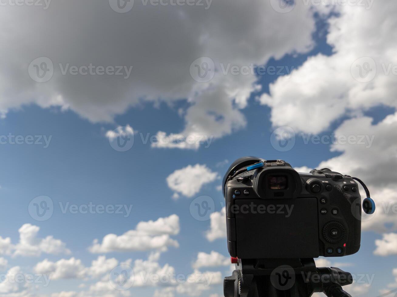 black professional digital camera on a tripod pointed at blue sky with white clouds photo