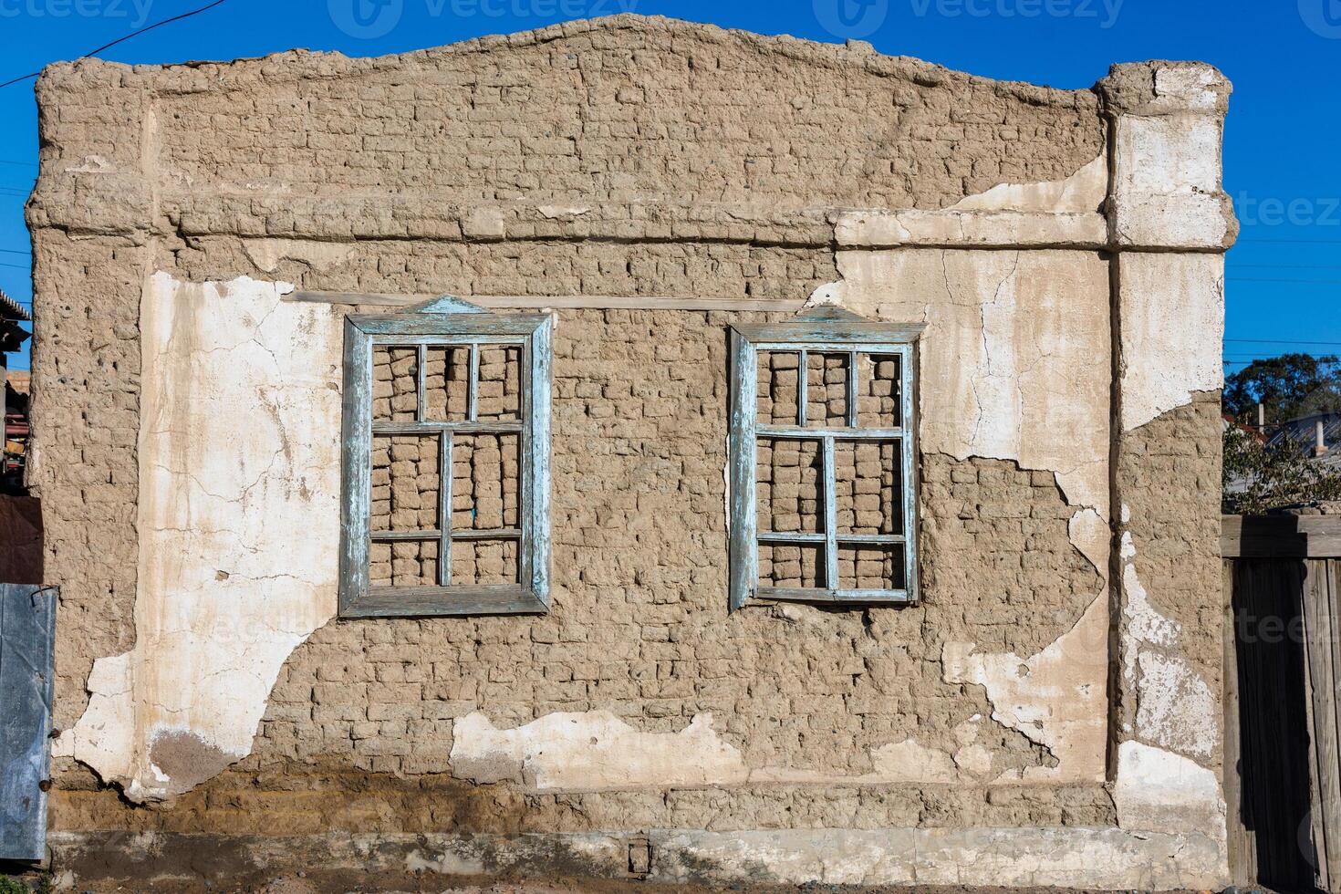 old house adobe air brick wall with two embedded wooden window frames and peeled off plaster leftovers - flat texture photo