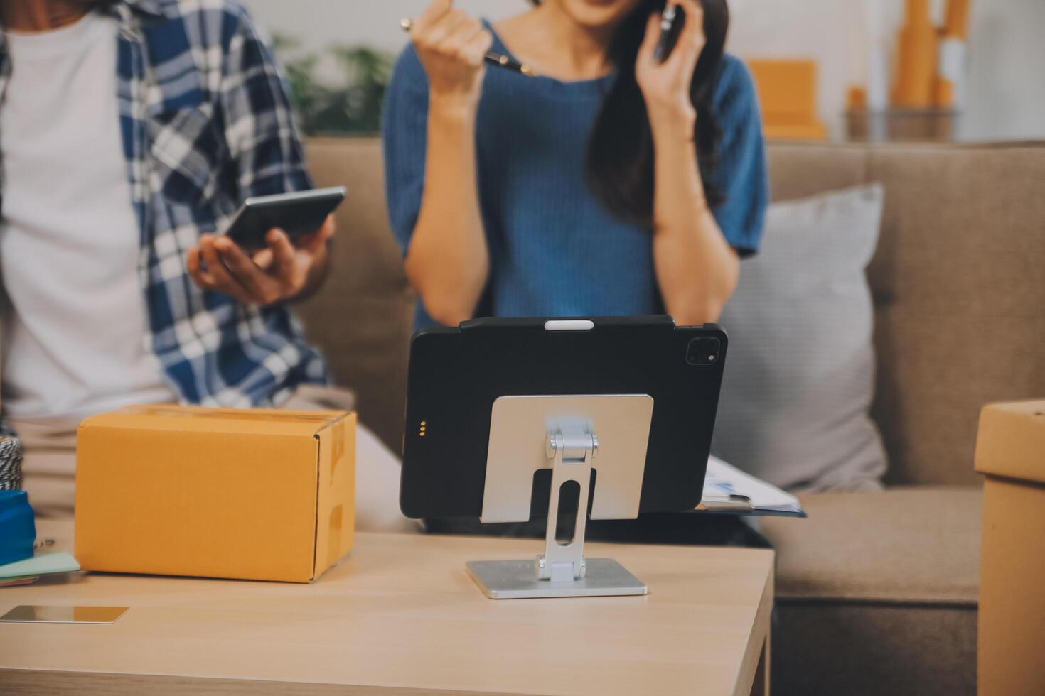 Two Asian blogger showing clothes in front of the camera to recording vlog video live streaming at her shop. Online Shopping Cart notion. on sofa at home photo