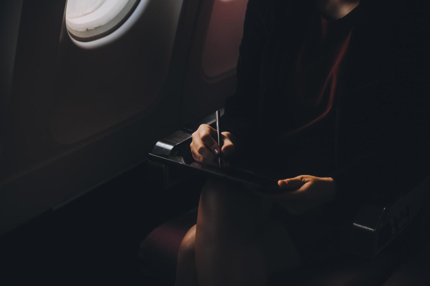 Blonde female tourist checking incoming notification on smartphone sitting on seat of airplane with netbook.Young businesswoman share media from telephone on laptop computer during plane flight photo