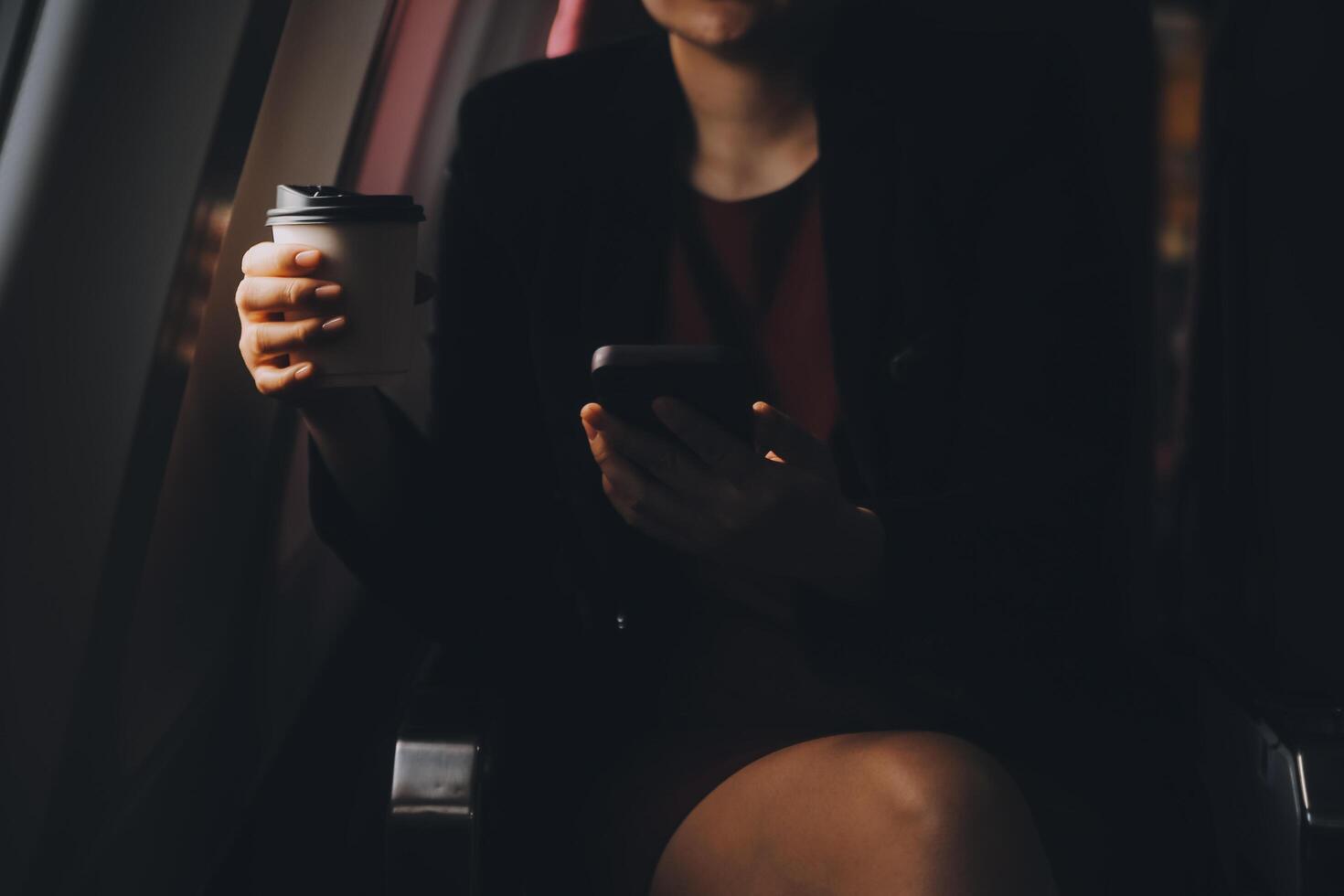Blonde female tourist checking incoming notification on smartphone sitting on seat of airplane with netbook.Young businesswoman share media from telephone on laptop computer during plane flight photo