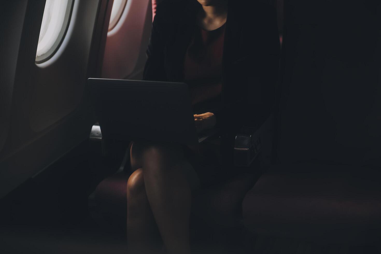 Blonde female tourist checking incoming notification on smartphone sitting on seat of airplane with netbook.Young businesswoman share media from telephone on laptop computer during plane flight photo