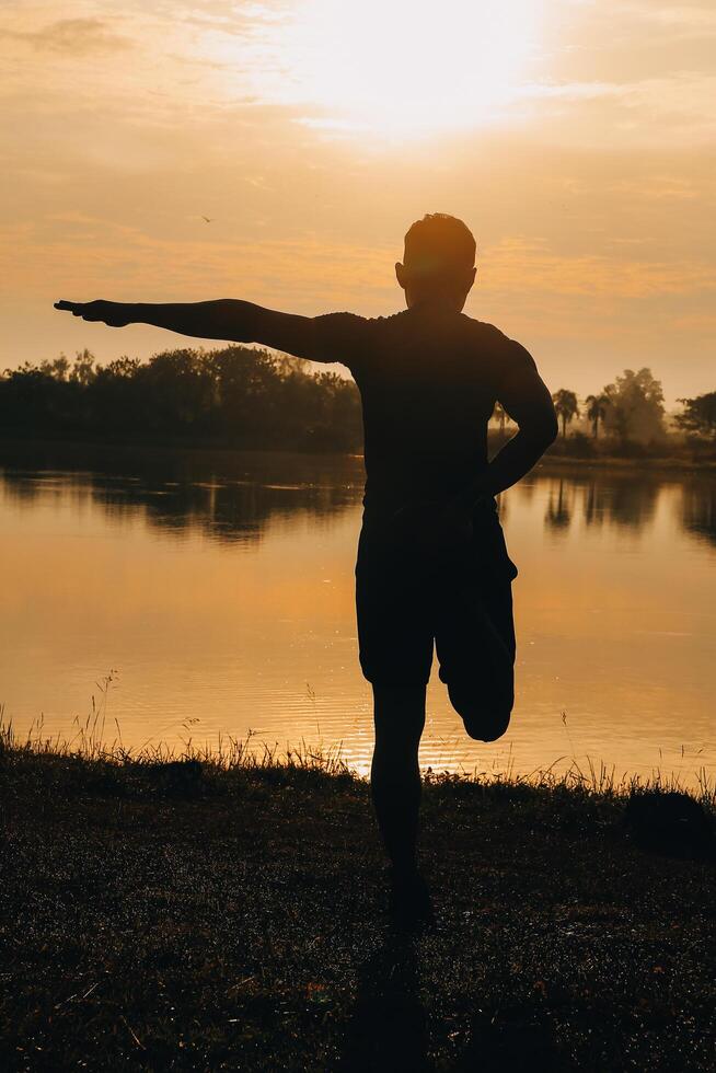 Back view silhouette of a runner man running on the beach at sunset with sun in the background photo